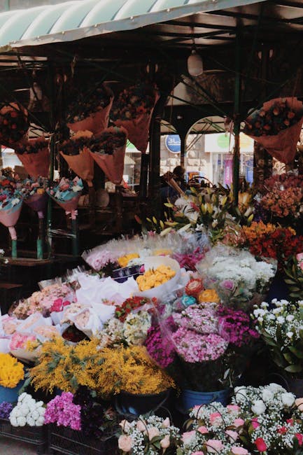 A vibrant display of fresh flowers arranged in a bouquet, featuring pink and yellow tulips with smooth, elongated petals and green leaves, alongside clusters of pink and yellow roses with layered peta